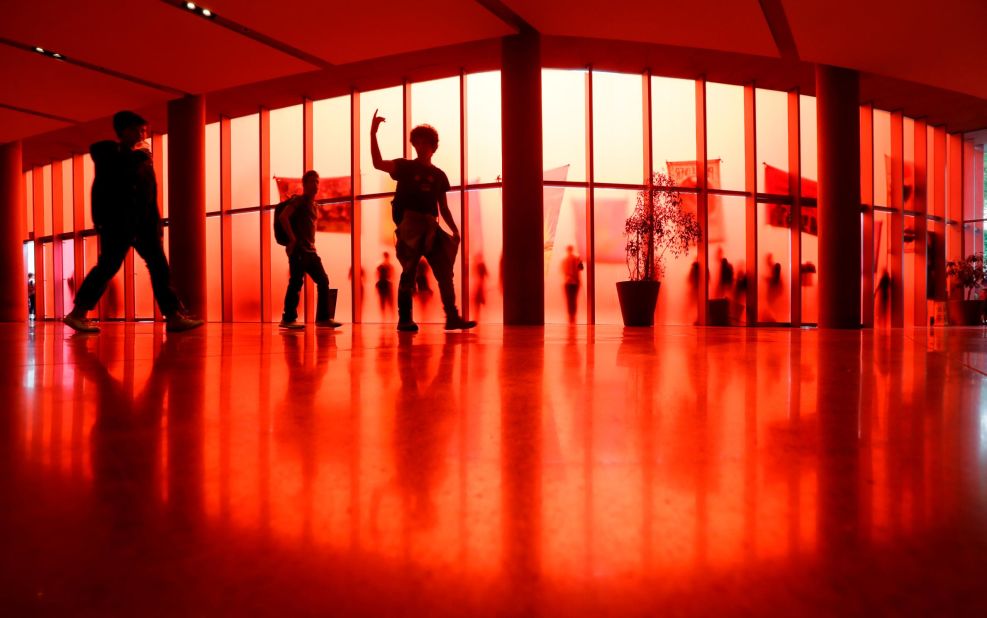 A student leads others to an exit past the translucent red walls of Seattle City Hall, while student climate activists protest outside.