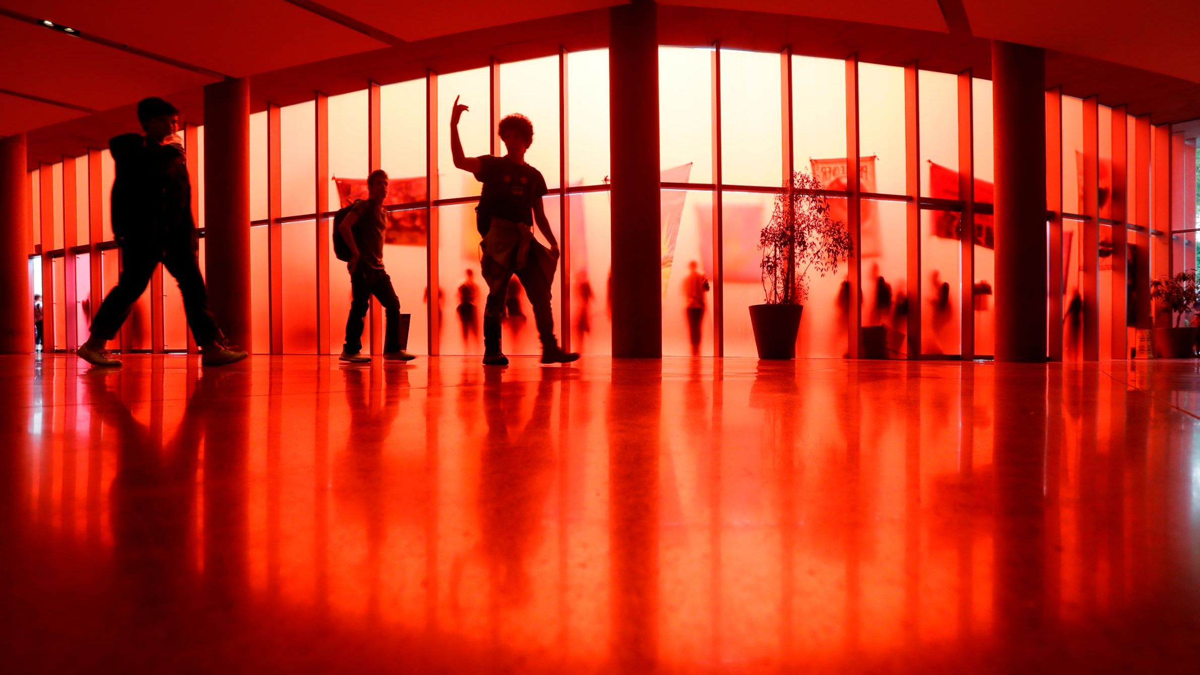 A student leads others to an exit past the translucent red walls of Seattle City Hall, while student climate activists protest outside.