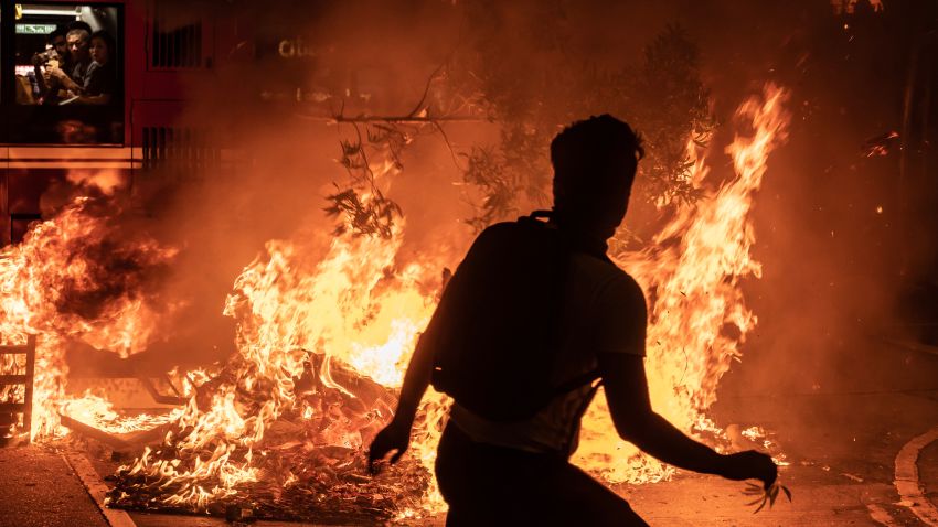 HONG KONG, CHINA - SEPTEMBER 22: A pro-democracy protester throws a tree branch at a burning barricade outside of the Mongkok Police Station as a bus drives in front of it on September 22, 2019 in Hong Kong, China. Pro-democracy protesters have continued demonstrations across Hong Kong, calling for the city's Chief Executive Carrie Lam to immediately meet the rest of their demands; including an independent inquiry into police brutality, the retraction of the word riot to describe the rallies, and genuine universal suffrage as the territory faces a leadership crisis. (Photo by Anthony Kwan/Getty Images)