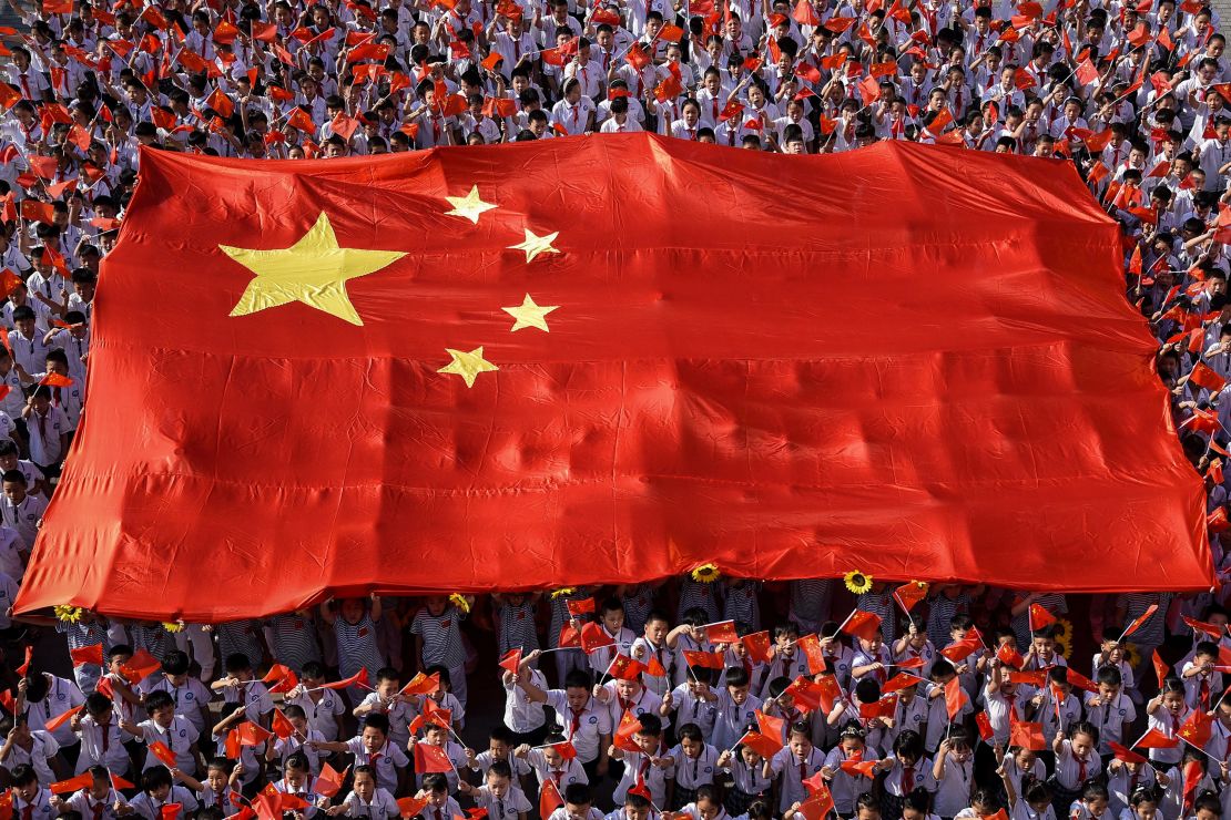 This photo taken on September 1, 2019, shows elementary school students waving national flags as they sing a patriotic song on the first day of the new semester in Handan in China's northern Hebei province.