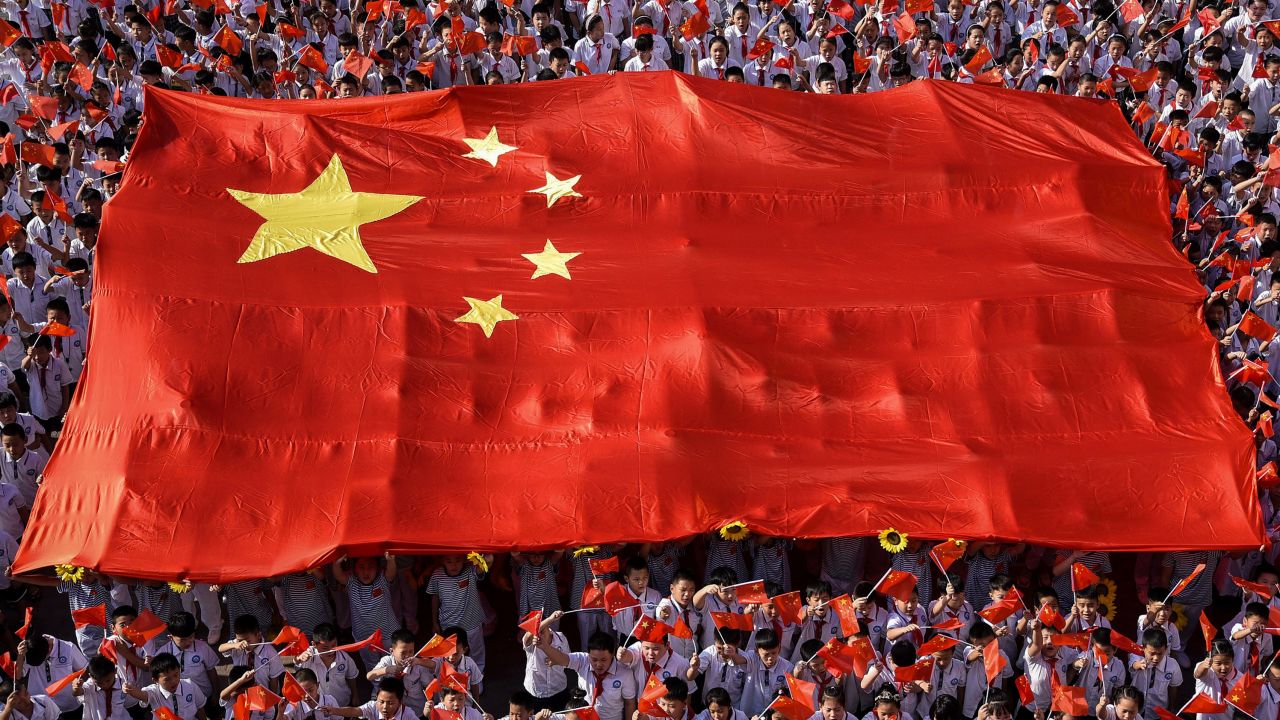 This photo taken on September 1, 2019, shows elementary school students waving national flags as they sing a patriotic song on the first day of the new semester in Handan in China's northern Hebei province.