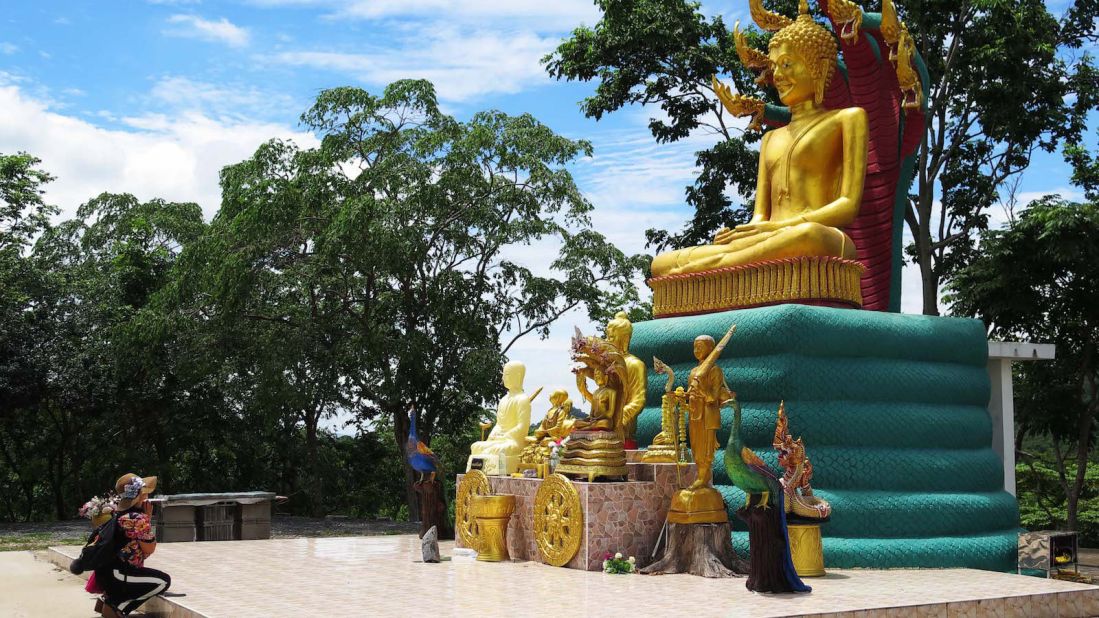 <strong>Hilltop Buddha: </strong>A Buddhist Thai woman kneels at a larger-than-life statue portraying Buddha protected by a mythical seven-headed "naga" snake, which has topped the hill for many years and was not associated with any UFOs before the family's tales. 