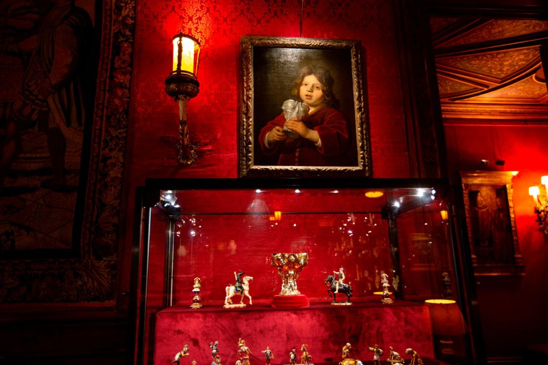 A painting of a boy holding a silver cup hangs above the cup itself.