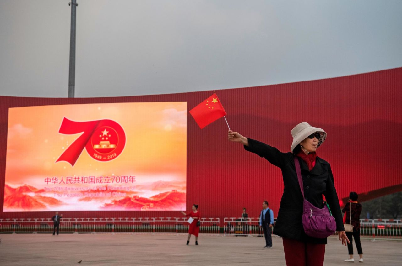 A Chinese woman holds a national flag near a large screen set up for the 70th National Day celebrations as they visit Tiananmen Square on September 27.
