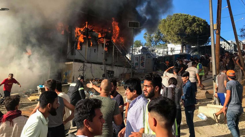Migrants and refugees stand next to burning house containers at the Moria refugee camp, on the northeastern Aegean island of Lesbos, Greece, Sunday, Sept. 29, 2019. Migrants protesting at an overcrowded camp on the Greek island of Lesbos set fires and clashed with police Sunday, authorities said. Police and local authorities said there were unconfirmed reports of two fatalities at the Moria camp. (InTime News via AP)