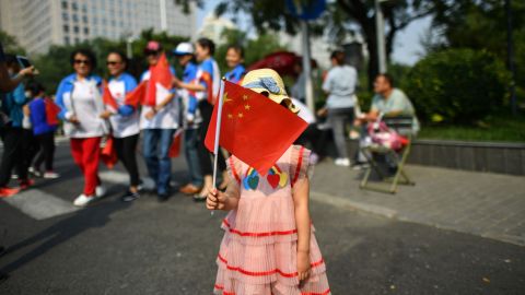 A girl holds a Chinese flag as people watch a military parade along the security perimeter established around the official ceremony in Tiananmen Square.