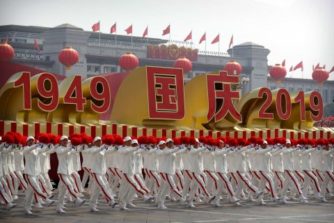 Participants wave flowers as they march next to a float commemorating the 70th anniversary of the founding of Communist China.