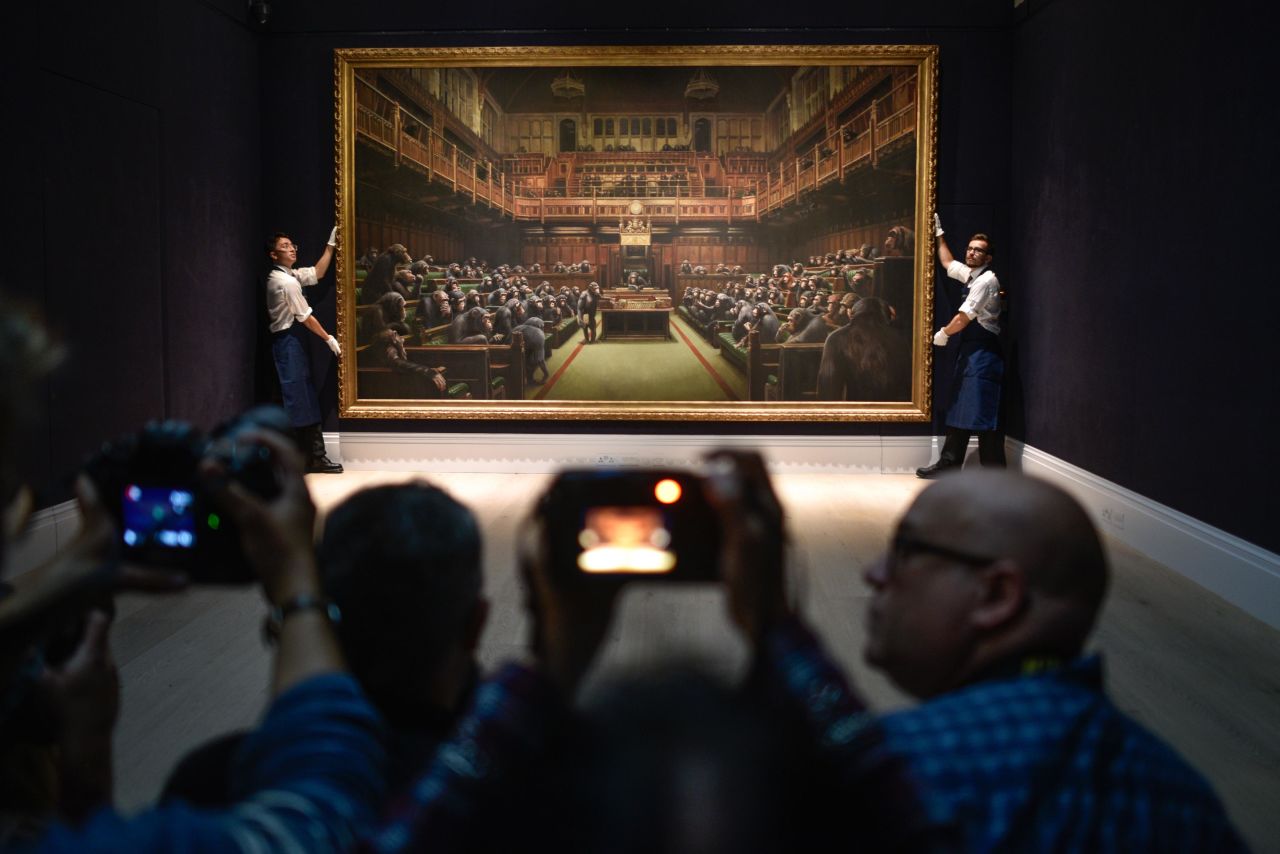 Gallery assistants pose with the Banksy painting "Devolved Parliament" at the Sotheby's auction house in London on Friday, September 27. <a href="https://www.cnn.com/style/article/banksy-devolved-parliament-gbr-scli-intl/index.html" target="_blank">The artwork </a>shows the benches of Parliament occupied by primates. 