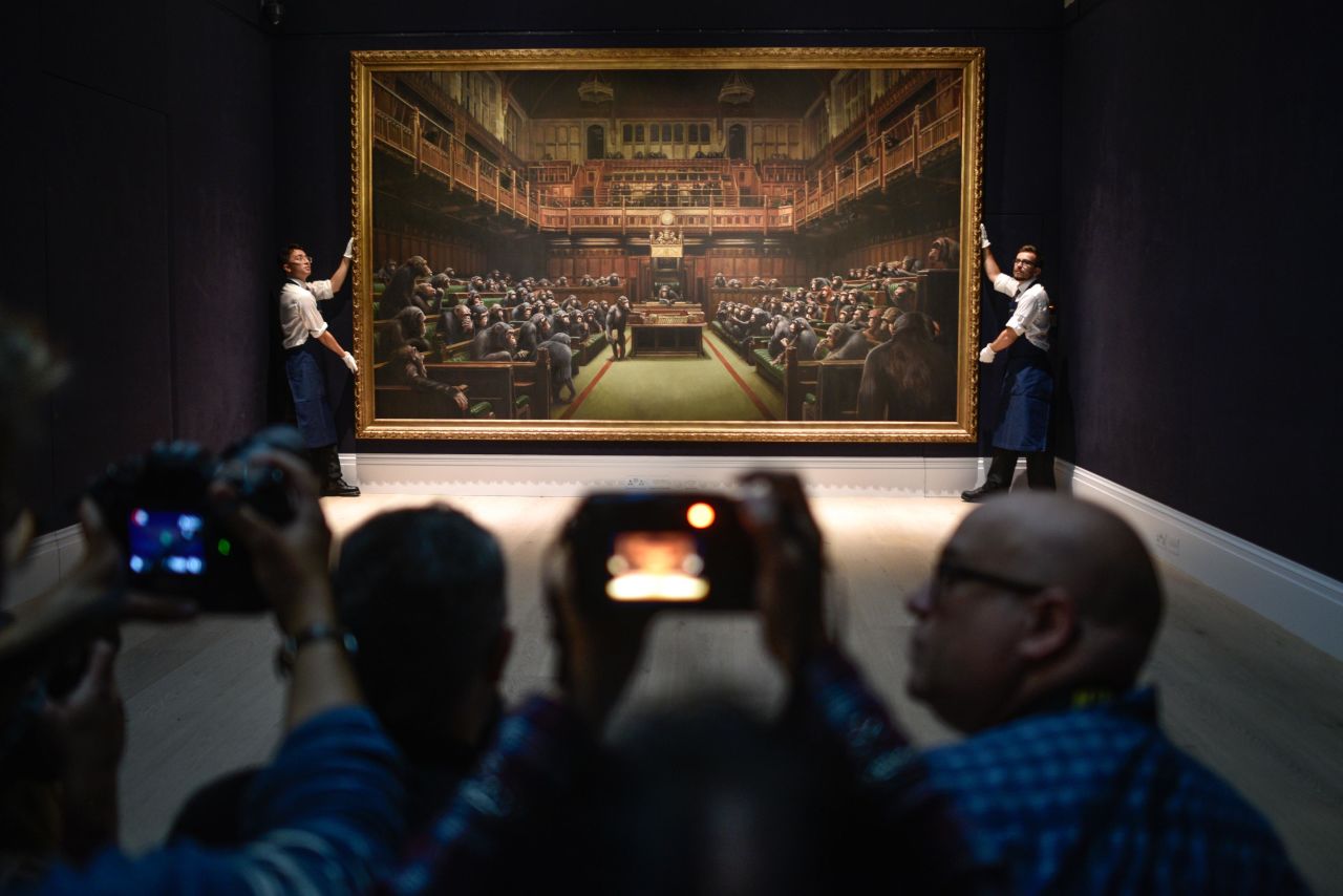 Gallery assistants pose with the Banksy painting "Devolved Parliament" at the Sotheby's auction house in London on Friday, September 27. <a href="https://www.cnn.com/style/article/banksy-devolved-parliament-gbr-scli-intl/index.html" target="_blank">The artwork </a>shows the benches of Parliament occupied by primates.