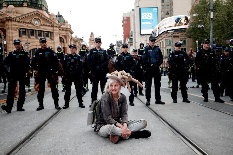 A woman sits down in front of a line of police in Melbourne.