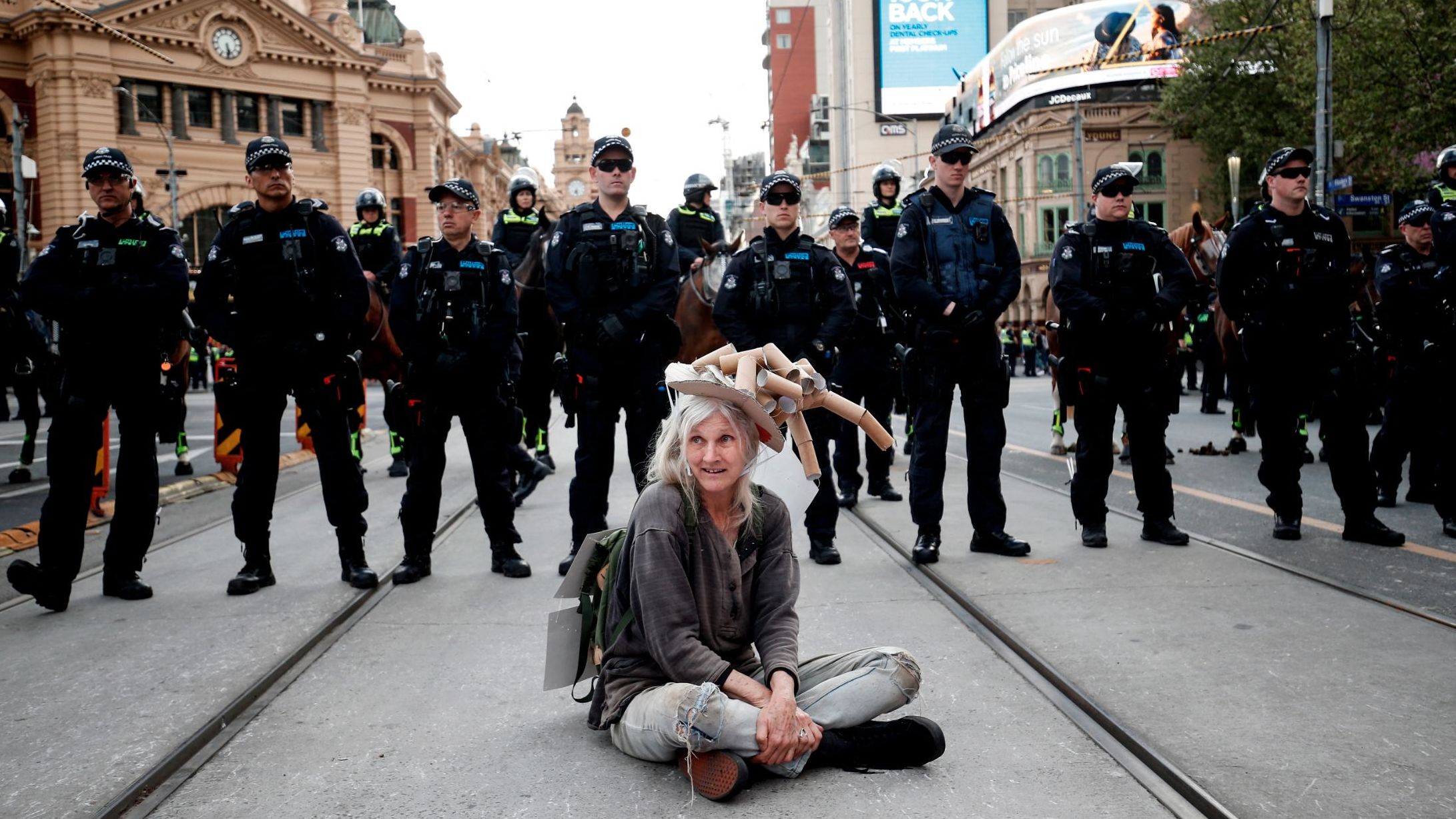 A woman sits down in front of a line of police in Melbourne.