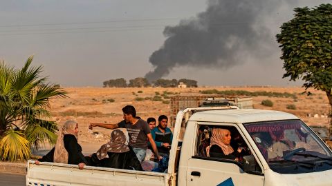 Civilians ride a pickup truck as smoke billows following Turkish bombardment on Syria's northeastern town of Ras al-Ain.