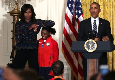 First lady Michelle Obama rests her elbow on Biles' head as President Barack Obama speaks during an Olympic athletes event at the White House in September 2016.