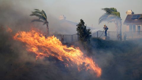 A firefighter sprays water in front of an advancing wildfire Friday, Oct. 11, 2019, in Porter Ranch, Calif.