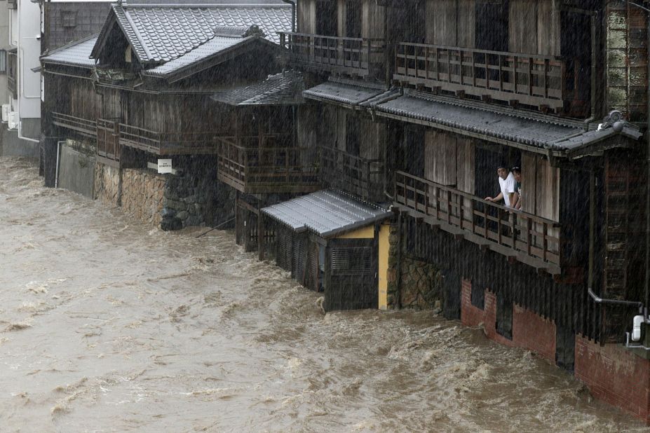 People watch floodwater from the Isuzu river flow by in Ise, Japan, on Saturday, October 12, 2019.