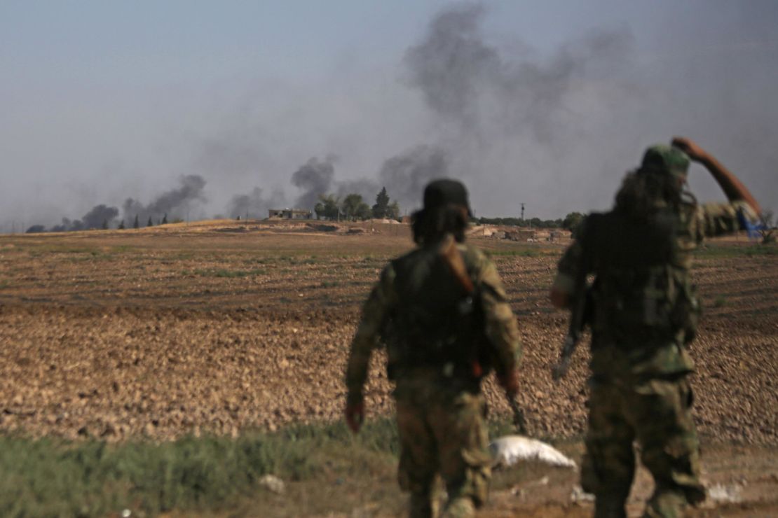 Turkish-backed Syrian fighters watch as smoke billows from the Syrian border town of Tal Abyad.