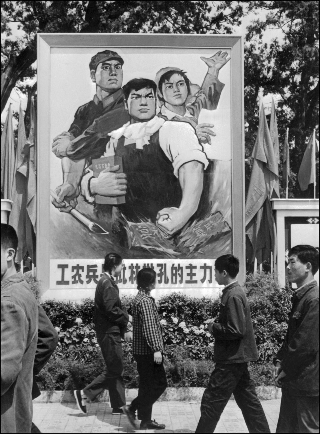 Beijing residents pass by a huge poster depicting two workers and one soldier. The poster reads, "Workers, peasants and soldiers are the principal force in the fight against Lin Biao and Confucius" in May 1974. 