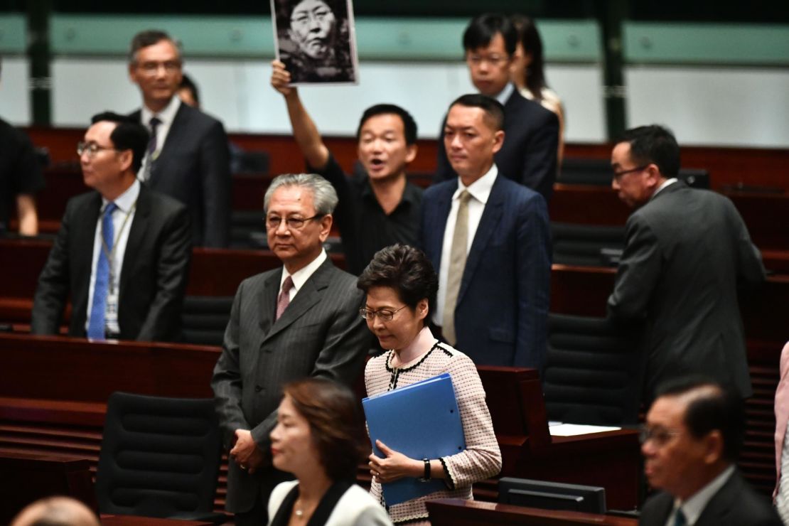 A pro-democracy lawmaker (behind) holds up a placard in protest as Hong Kong's Chief Executive Carrie Lam (C) walks into the chamber to give her annual policy address at the Legislative Council (Legco) in Hong Kong on October 16, 2019. 