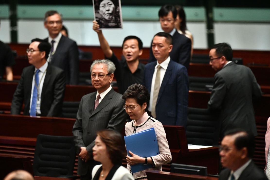 A pro-democracy lawmaker (behind) holds up a placard in protest as Hong Kong's Chief Executive Carrie Lam (C) walks into the chamber to give her annual policy address at the Legislative Council (Legco) in Hong Kong on October 16, 2019.