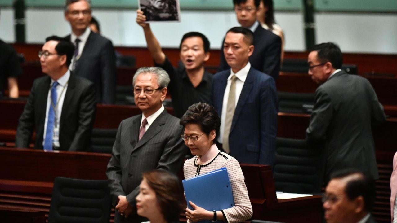 A pro-democracy lawmaker (behind) holds up a placard in protest as Hong Kong's Chief Executive Carrie Lam (C) walks into the chamber to give her annual policy address at the Legislative Council (Legco) in Hong Kong on October 16, 2019. 