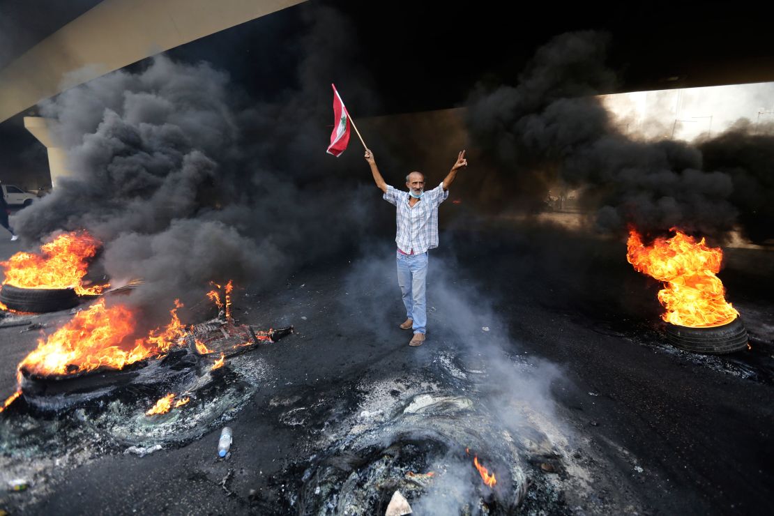 An anti-government protester makes a victory sign, while holding a Lebanese flag and walking past blazing tires during a protest on October 18.