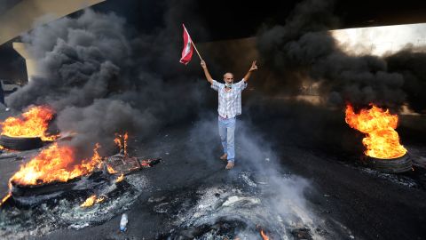 An anti-government protester makes a victory sign, while holding a Lebanese flag and walking past blazing tires during a protest on October 18.