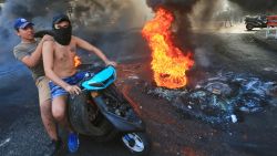 Lebanese demonstrators drive past a tire fire during a protest against dire economic conditions in the Lebanese capital Beirut's southern suburbs on October 17, 2019. - Public anger has simmered since parliament passed an austerity budget in July to help trim a ballooning deficit and flared on Thursday over new plans to tax calls on messaging applications such as Whatsapp, forcing the government to axe the unpopular proposal.