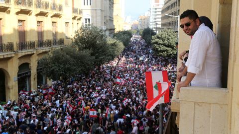 A man holds a Lebanese flag as he stands on a balcony during a protest.