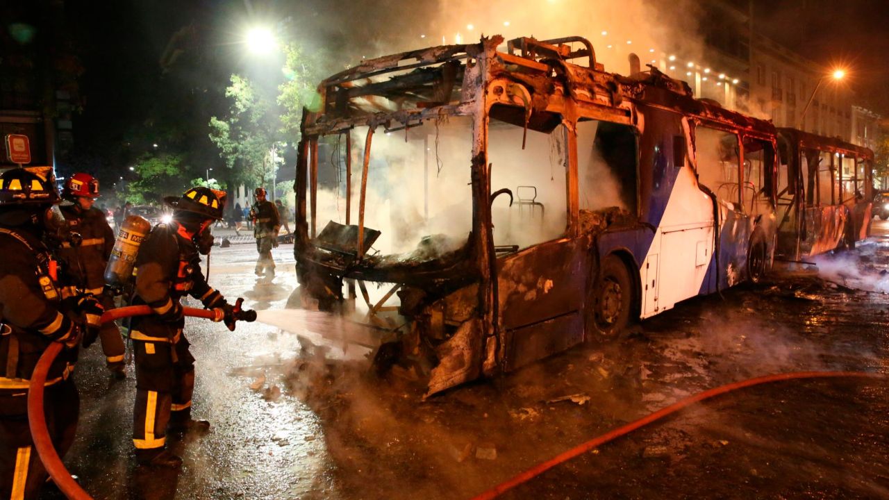 Firefighters put out the flames on a burning bus during a protest in Santiago, Friday, October 18, 2019.