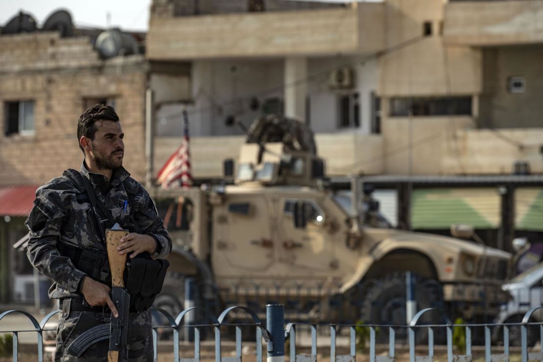 A fighter from the Syrian Democratic Forces SDF stands guard as a US military vehicle pulling out of a US forces base in the Northern Syrian town of Tal Tamr drives by.