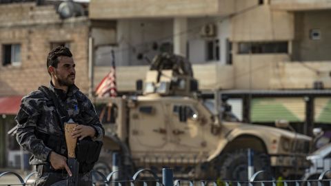 A fighter from the Syrian Democratic Forces SDF stands guard as a US military vehicle pulling out of a US forces base in the Northern Syrian town of Tal Tamr drives by.