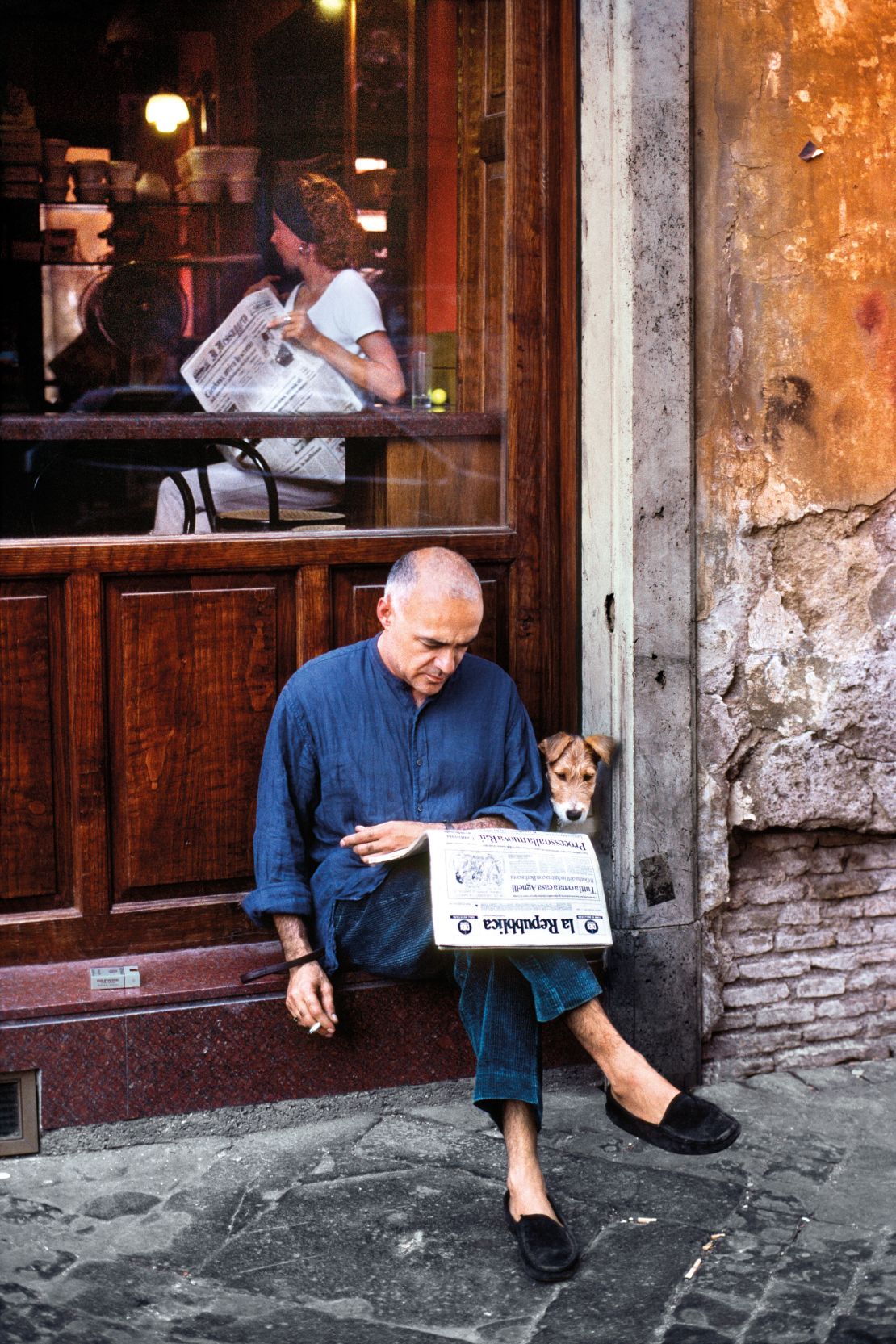 A man reads the newspaper with his dog outside a restaurant in Rome, Italy, 1994.