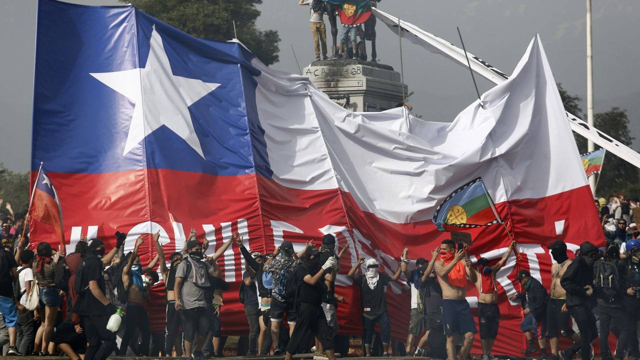 SANTIAGO, CHILE - OCTOBER 23: Demonstrators spread a giant flag of Chile as they gather at Plaza italia against President Sebastian Pi?era during the sixth day of protest against President Sebastian Pi?era on October 23, 2019 in Santiago, Chile. Although President Sebastian Pi?era announced yesterday a few measures to improve equality, unions called for a national strike and demonstrations continue as casualties are now 18. Demands behind the protest include issues like health care, pension system, privatization of water, public transport, education, social mobility and corruption. (Photo by Marcelo Hernandez/Getty Images)