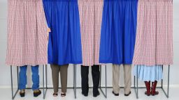 A row of five voting booths with men and women casting their ballots at a polling place. Horizontal format, only showing the legs of the voters, people are unrecognizable..; Shutterstock ID 114656170; Job: -