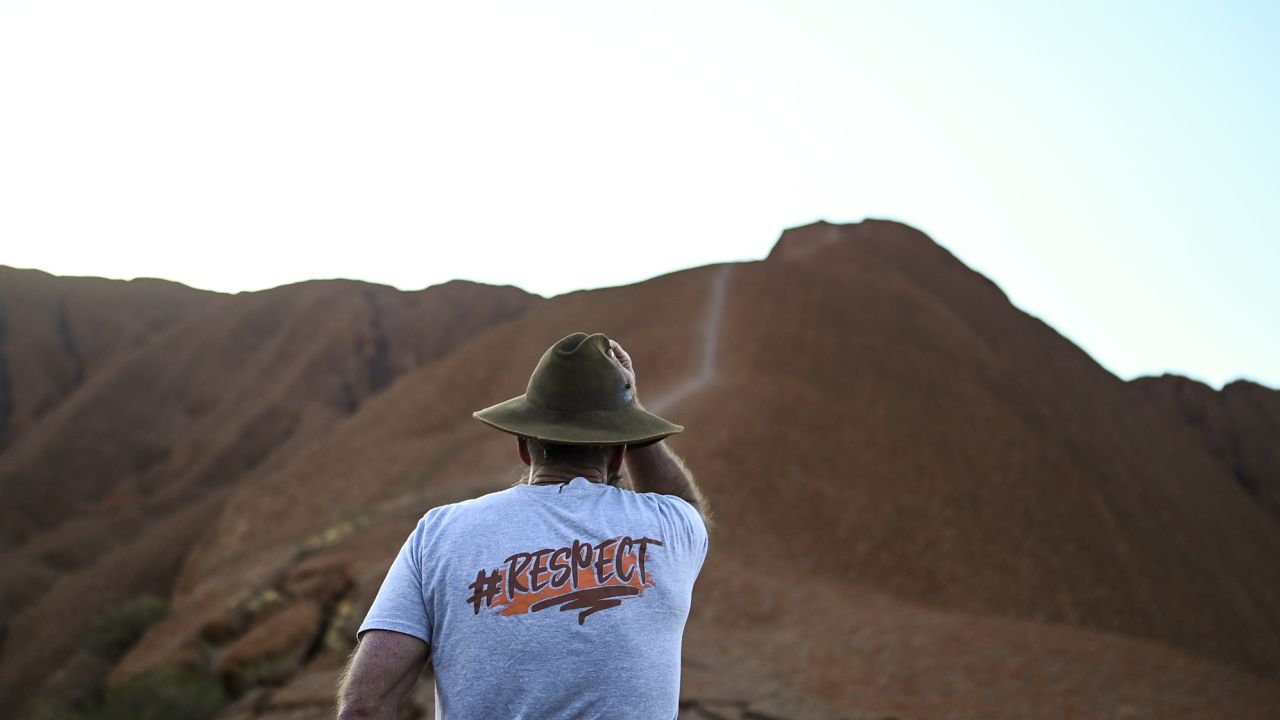 A man wearing a t-shirt saying 'I chose not to climb' stands next to tourists lining up to summit Uluru on October 25. 