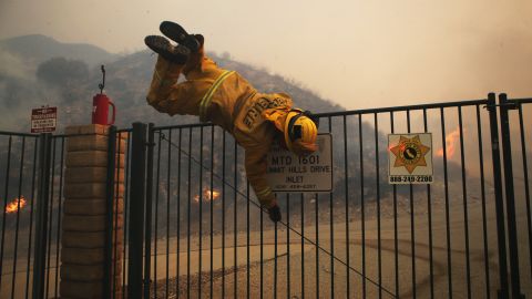 A Cal Fire firefighter hops over a locked gate while working the Tick Fire on Thursday in Canyon Country, California. 