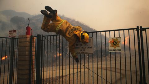 A Cal Fire firefighter hops over a locked gate while working the Tick Fire on Thursday in Canyon Country, California.