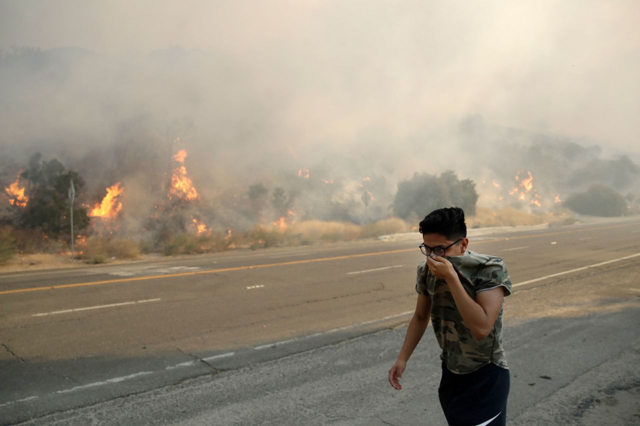 Brandon Mani covers his face from the smoke as he walks along Highway 14 in Santa Clarita.