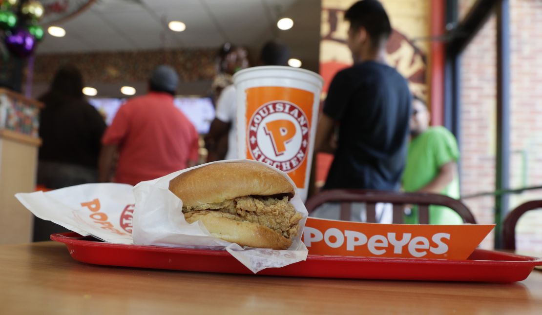 A chicken sandwich sits on a table at a Popeyes as guests wait in line.