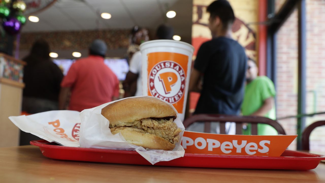A chicken sandwich sits on a table at a Popeyes as guests wait in line.