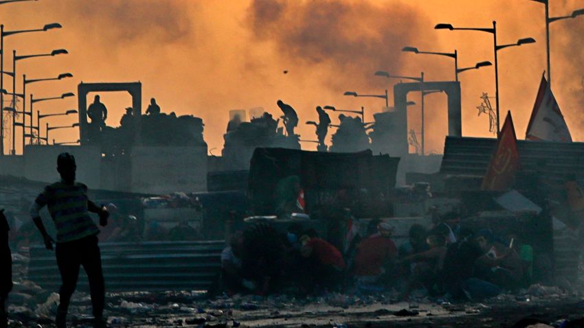 Anti-government protesters take cover while Iraqi security forces, back, fire tear gas and close the bridge leading to the Green Zone, during a demonstration at sunset in Baghdad, Iraq, Sunday, Oct. 27, 2019. Protests have resumed in Iraq after a wave of anti-government protests earlier this month were violently put down. (AP Photo/Khalid Mohammed)