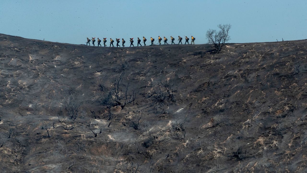 Fire crews walk along a blackened ridge as they battle the Getty Fire in Los Angeles.