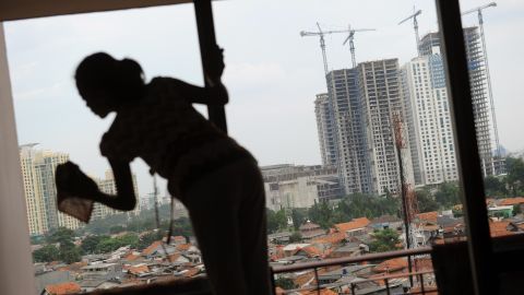 A house maid cleans an apartment window in Jakarta while a construction site for high rise commercial and residential buildings are seen in the background.
