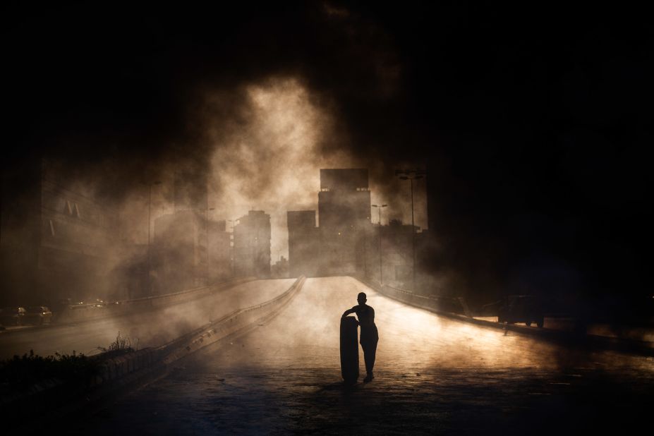 A protester rolls a tire toward a smoking roadblock in Beirut on Friday, October 18.