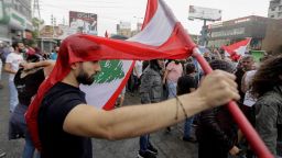 A Lebanese protester uses a national flag to protect himself from the rain on October 23, 2019, in the area of Zouk Mosbeh north of the capital Beirut. - Tens of thousands of Lebanese protesters kept the country on lockdown, rallying for a sixth consecutive day to demand new leaders despite the government's adoption of an emergency economic rescue plan. Demonstrations initially sparked by a proposed tax on WhatsApp and other messaging apps quickly grew into an unprecedented cross-sectarian street mobilisation against the political class. (Photo by JOSEPH EID / AFP) (Photo by JOSEPH EID/AFP via Getty Images)