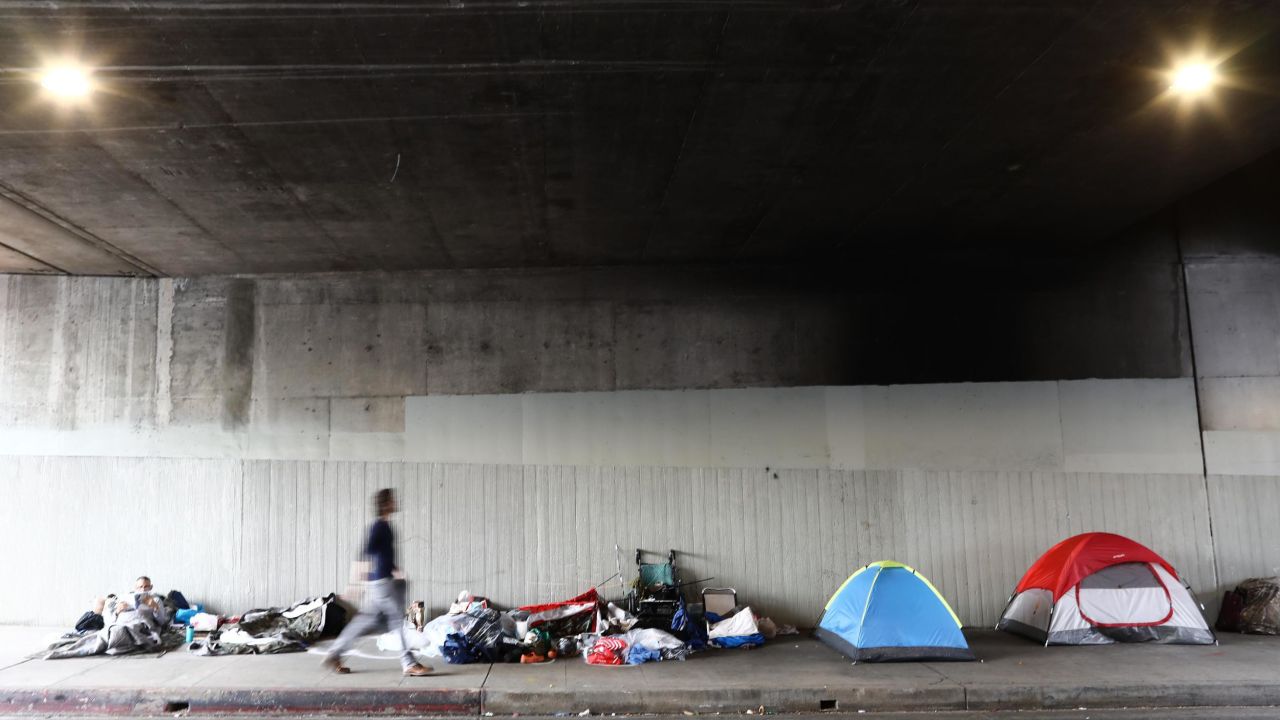  A man walks past a homeless encampment beneath an overpass in Los Angeles, California.