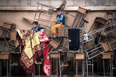 Displaced Syrian children sit on classroom tables at a school turned into a shelter on Thursday, October 24.