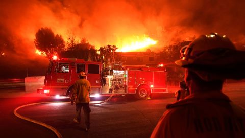 Los Angeles County firefighters look on as the out of control Woolsey Fire explodes behind a house in the West Hills neighborhood.