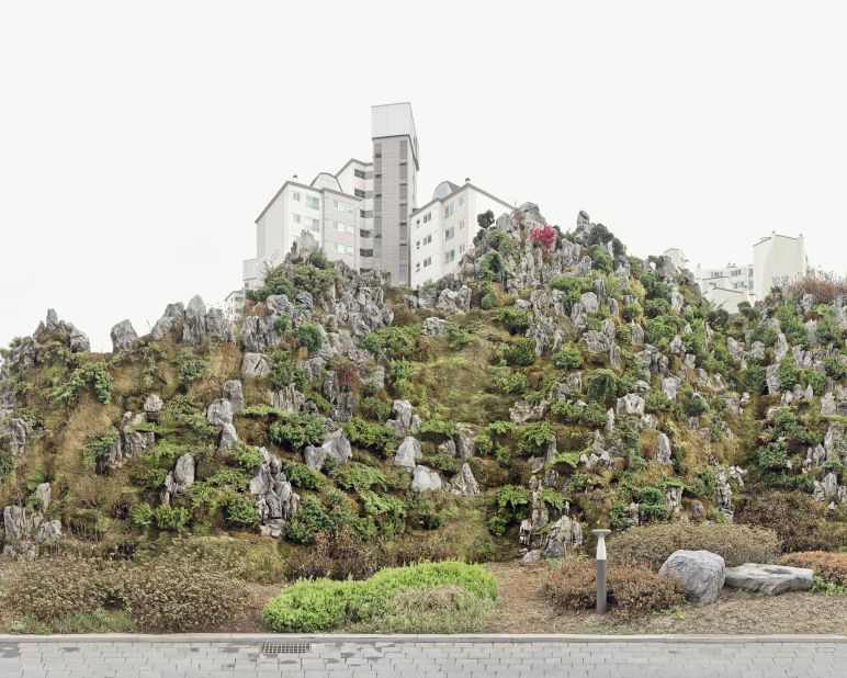 Workers build a basic styrofoam mold, which is secured on, or around, the apartment block. They then cover it with soil, before planting flowers and trees to mimic a real-life mountainside.