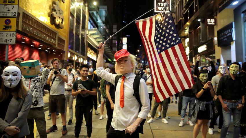 A person dressed as President Donald Trump waves an American flag as they stand on a street in Hong Kong, Thursday, Oct. 31, 2019. Hong Kong authorities are bracing as pro-democracy protesters urged people on Thursday to celebrate Halloween by wearing masks on a march in defiance of a government ban on face coverings. (AP Photo/Kin Cheung)